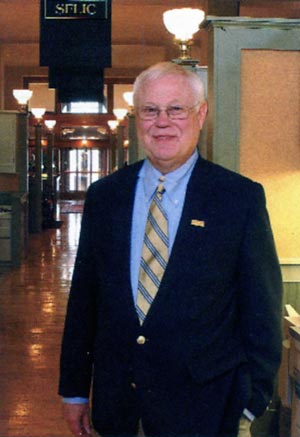 Courtney Crouch, SFLIC President, stands beneath a banner declaring the company’s 40th Anniversary. Their corporate office is housed in the restored Hot Springs National Park Post Office, across the street from the Hot Springs Convention Center.